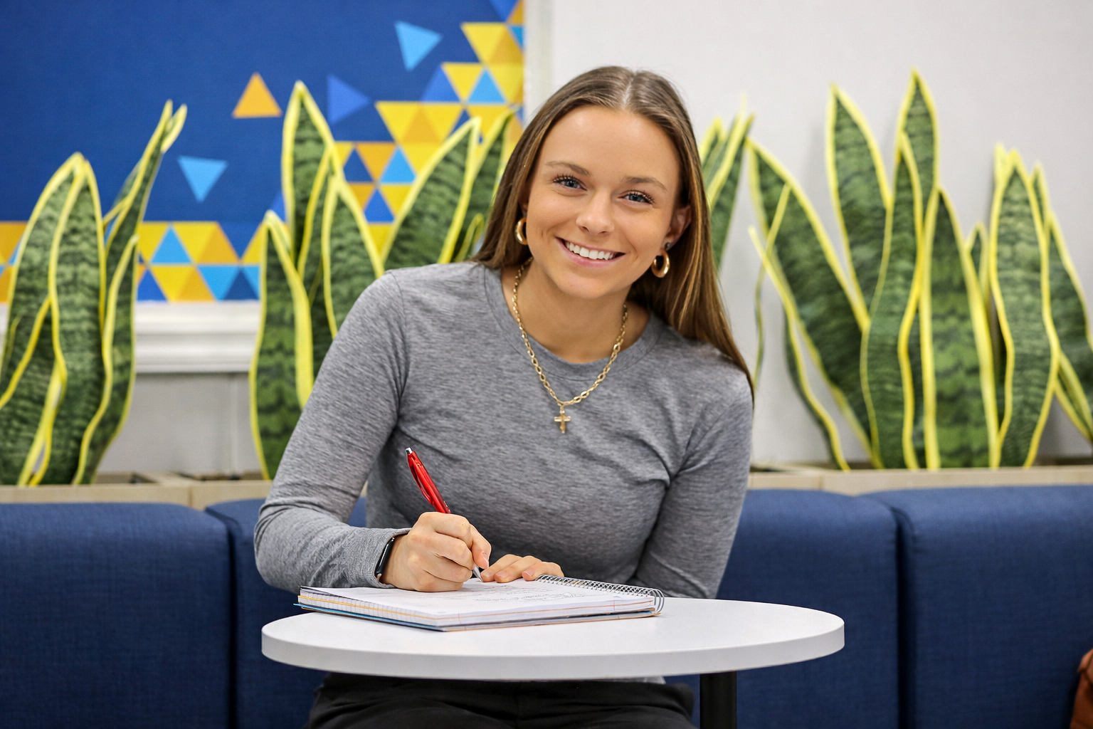a student sitting at a table smiling with pen and notebook