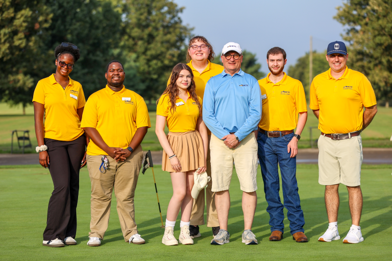 a group photo of students and the chancellor on a golf course