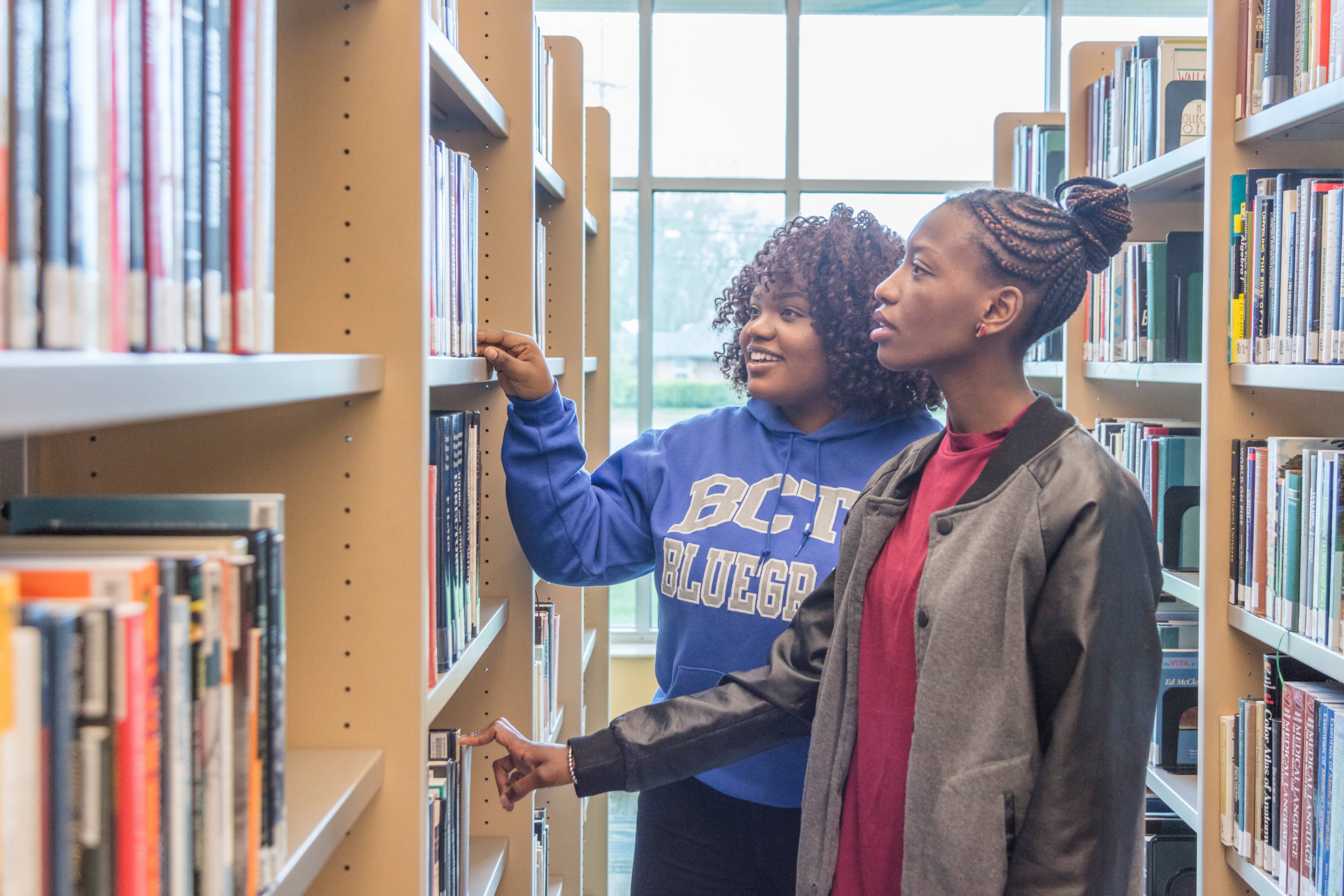 2 students looking at books on a library shelf