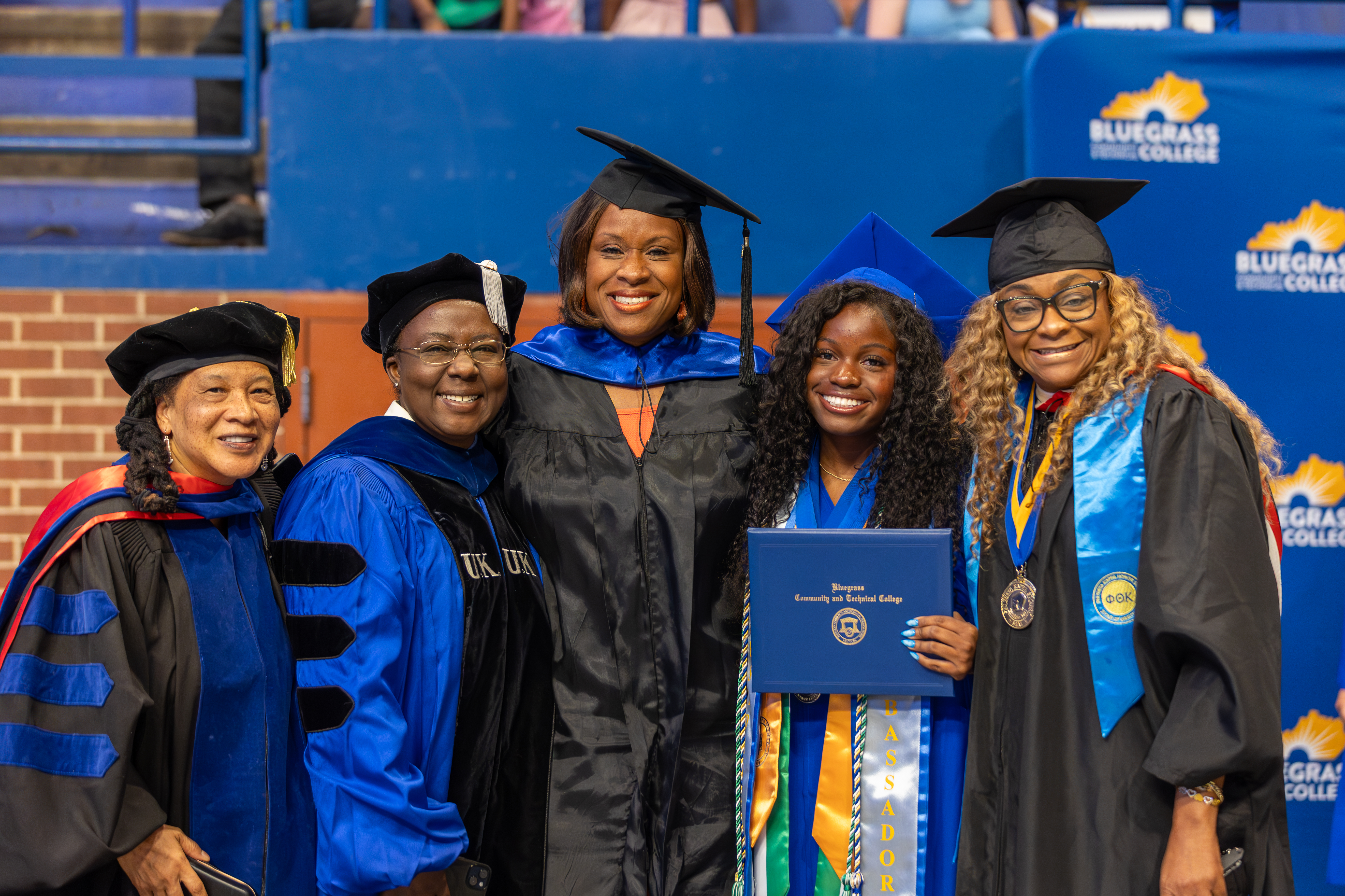 faculty members pose with graduate at commencement ceremony