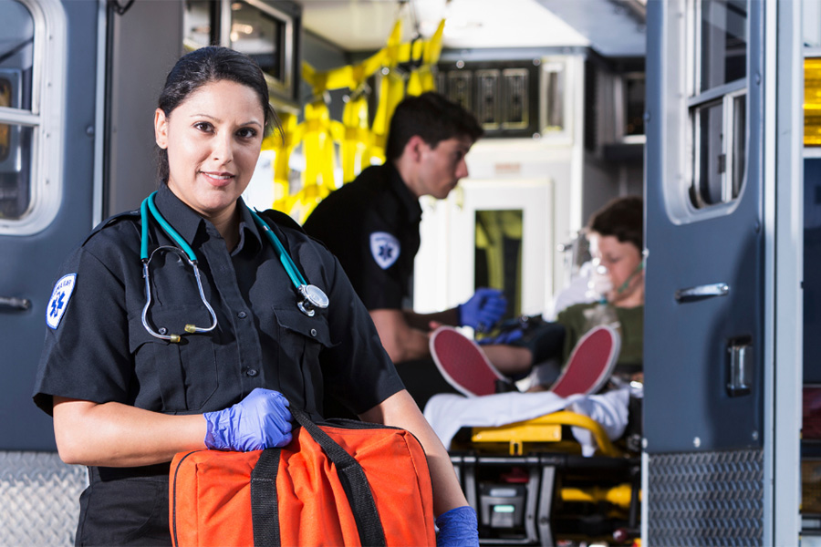 Paramedic smiling at camera with another paramedic and patient in back of ambulance behind her