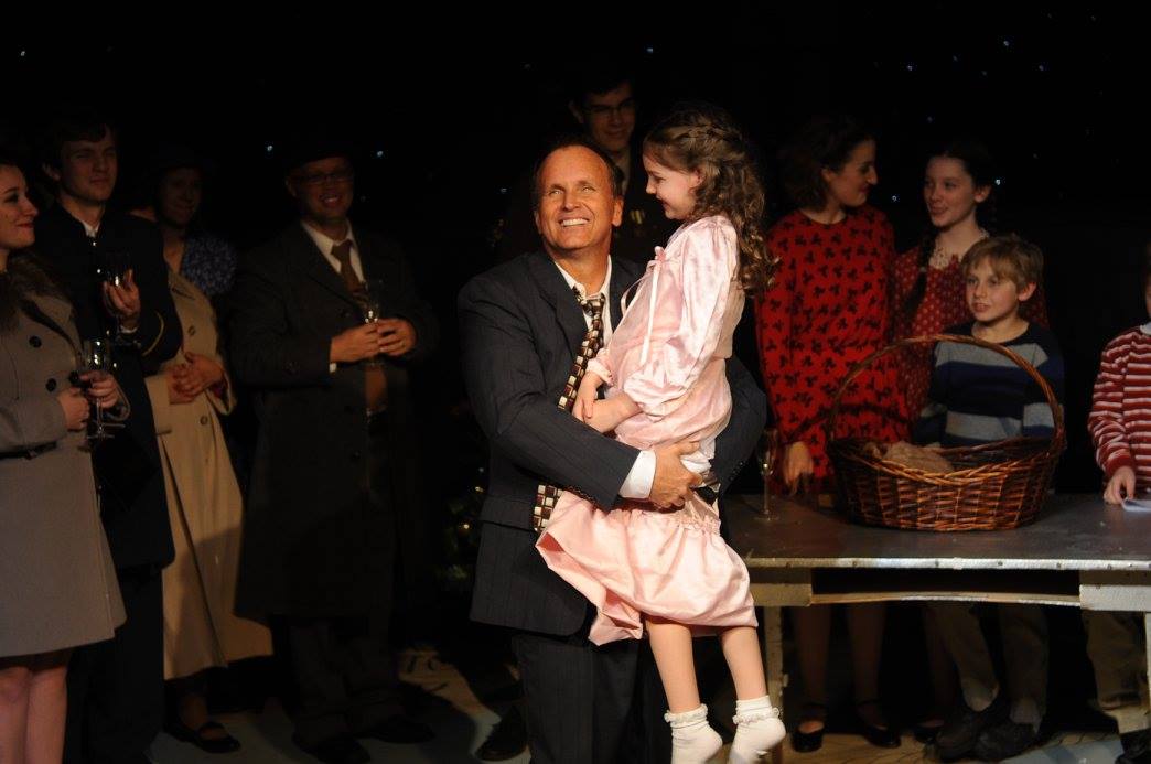 person smiling holding child with people in background