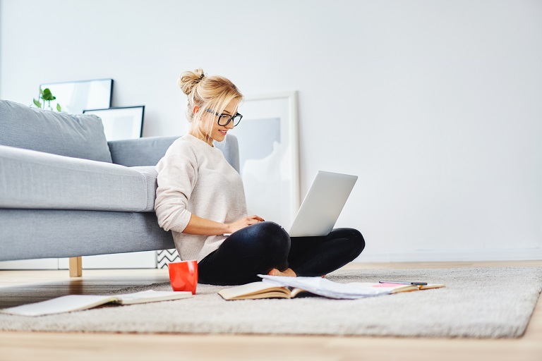 Woman sitting in her living room floor working on classes.