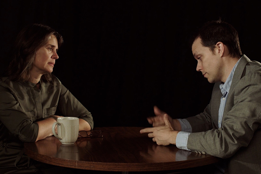 A scene from the FLM 190 film where two people converse at a table in a dim room