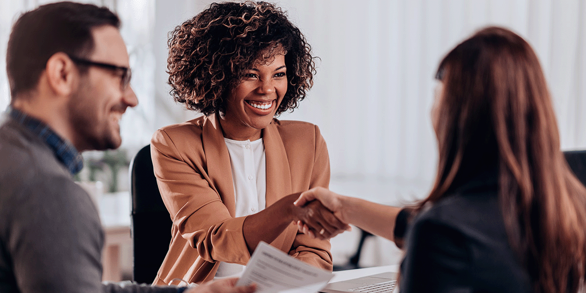 two people shaking hands during meeting while another holds a resume